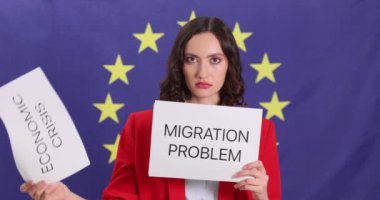 Kadının elinde Avrupa Birliği bayrağına karşı ülkenin acil sorunlarıyla dolu kartlar var. Kadın, yabancı ülkede yaşamanın zorluklarına dikkat çekiyor