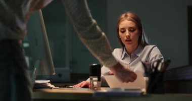 Erkek iş arkadaşı iş belgelerini getirirken, iş kadını masa başında oturuyor. Çok çalışan kadın çalışanlar ofiste yavaş çekimde kağıt parçalarını kırıştırıyor.