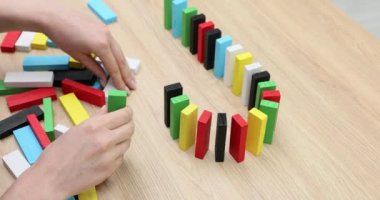 Kadın masadaki tahta blokları kullanarak renkli domino taşları inşa ediyor. Canlı kurulum, zincirleme reaksiyon için yavaş çekim düzenleme yeteneğini gösterir.