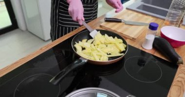Şef pembe eldiven takıyor ve patates kızartmasını tavada doğruyor. İnsan lezzetli bir kahvaltı hazırlamak için spatula ve sebze malzemesi kullanır.