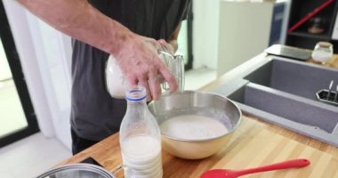 Erkek şef cam kavanozdan süt dolu metal kaseye un döker. İnsan ahşap mutfak tezgahında, pişirme sanatını ön plana çıkaran bir karışım yaratır.