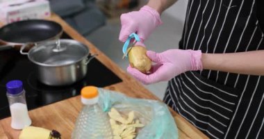 Mutfakta çiğ patatesleri soyar ve yemek hazırlamaya odaklanır. Sahne, aşçılık becerisi ve taze malzemeler pişirme sanatını ön plana çıkarıyor