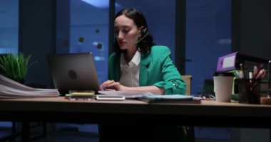 Kendini işine adamış bir profesyonel loş bir ofiste dizüstü bilgisayarına odaklanmış vazifelerine bağlılığını gösteriyor.