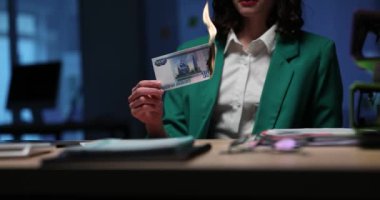 Bir ofiste, yeşil ceketli bir kişi dramatik bir şekilde bir banknotu tutuşturur ve güçlü bir görüntü yaratır.