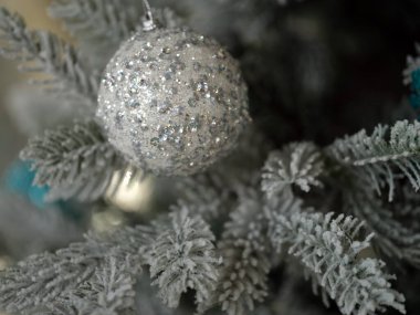 Zarif gümüş bir süs, güzelce süslenmiş, donuk bir Noel ağacına asılmış.