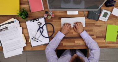 Erkek doktor masada oturur ve klavyede hastanın semptomlarını kaydeder. Nitelikli hekim hastanın tıbbi geçmişine yavaş çekimde bilgisayar veritabanına girdi