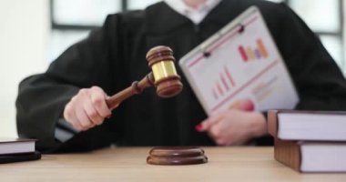 Önlüklü kadın yargıç, tahta masada oturan tokmağa vurdu. İstatistiksel veri içeren belgelere sahip kadın yargıç karar verdi