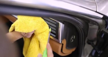 Adam yavaş çekimde torpido gözünde havalandırma ızgarasını özenle temizliyor. Sahibi yumuşak bez ve buhar temizleyicisi kullanarak otomobille ilgileniyor.