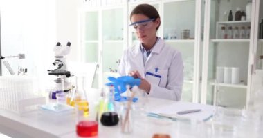 Kadın bilim adamı lastik eldivenleri giyip kimyasal analize hazırlanıyor. Araştırmacılar laboratuarda araştırma için steril ortamı korumak için eldiven kullanıyor.