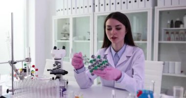 Yetenekli kadın kimyacı, molekül modelini elinde tutuyor. Genç dişi, molekülün yapay modelini gösteriyor ve derste yapıyı açıklıyor.
