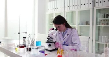 Genç kadın bilim adamı mikroskop altında numune üzerinde çalışıyor. Profesyonel araştırmacı sonuçların önemi üzerine kafa yorar. Kadın gözlemleri analiz eder.