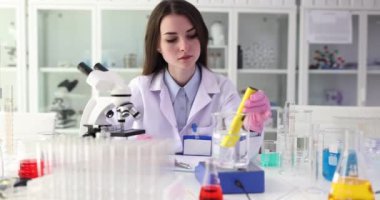 Deneyimli kadın laboratuvar teknisyeni, deney tüpündeki suyun pH seviyesini aletle ölçer. Profesyonel laboratuvar asistanı kesin sonuçları not defterine kaydeder.
