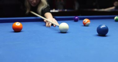 Odaklanmış sarışın bilardo oyuncusu bilardo topu kullanarak rafa vuruyor. Yetenekli kadınlar, mavi masalı kulüpte keyifli bilardo seanslarına katılırlar.