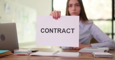 İş kadını, ofiste masasında duran sözleşmeli kağıtları gösteriyor. Katı yüz ifadesi olan bir kadın yasal olarak işbirliği sunar.