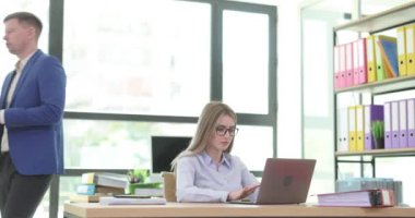 Genç bayan sekreter modern dizüstü bilgisayarda yazarken patron ofiste belge içeriğini dikte ediyor. Kadın, iş arkadaşının konuşmasını dikkatle dinler.