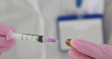 Pembe eldivenli asistan klinikteki cam şişeden yapılan aşıyı şırıngayla dolduruyor. Sağlık çalışanı hastane ofisinde enjeksiyon için ilaç hazırlar.