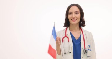 Mutlu bayan doktor beyaz arka planda Fransız bayrağı sallıyor. Gülümseyen kadın terapist ulusal tatilde neşe ve gurur yayıyor.