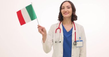 Pozitif kadın doktor beyaz arka planda İtalyan bayrağı sallıyor. Genç kadın sağlık çalışanı memnuniyet ve vatanseverliği ifade ediyor