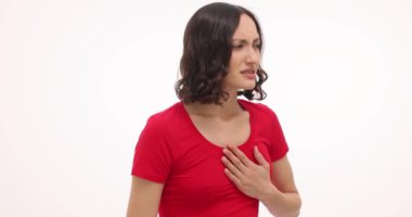 Esmer kadın beyaz arka planda göğüs ağrısından muzdarip. Kırmızı tişörtlü esmer kadın kalp ağrısından rahatsız olduğunu ifade ediyor.
