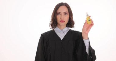 Kadın yargıç beyaz arka planda CBD yağ şişesi ve kelepçe gösteriyor. Esrar mevzuatını çevreleyen yasadışı faaliyetten hapis