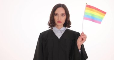 Siyah cüppeli ciddi yargıç beyaz arka planda gökkuşağı bayrağı ve kelepçe sallıyor. Kadın avukat LGBT toplumunu ayrımcılıktan korudu