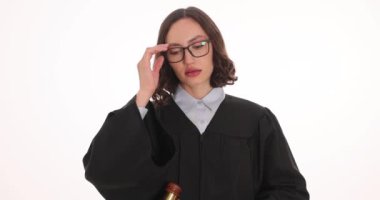 Yorgun kadın yargıç, beyaz arka planda şüphe uyandıran gözlükleri çıkarır. Tokmaklı kadın avukat duruşma sırasında tanık ifadelerini dinliyor.