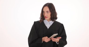 Kadın yargıç, beyaz arka plana bakarak dolar çantalarını bornoz koluna saklar. Adliyedeki yolsuzluk sorununun altını çizmek