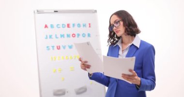 Şüpheli kadın öğretmen öğrencilerin çalışma belgelerini sınıflarda karşılaştırır. Pedagog, İngilizce alfabesiyle tahtadaki tutarsızlıkları kontrol ediyor
