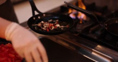 Şef mutfaktaki gaz sobasının yanındaki küçük tavaya sebze ve mantar döker. Eldivenli kişi akşam yemeği için lezzetli vegan yemeği pişirir.