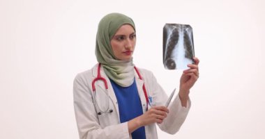 Türbanlı ciddi kadın doktor beyaz arka planda hastanın akciğerlerinin röntgen görüntüsünü inceliyor. Müslüman kadın klinikte göğüs resmini inceliyor