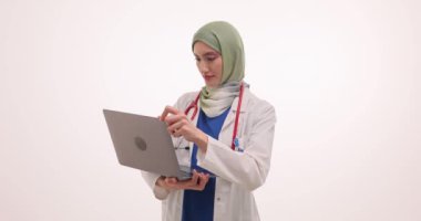 Müslüman kadın doktor, hastasını online randevuda dizüstü bilgisayarla karşılıyor. Üniformalı Arap kadın doktor el sallayarak bilgisayar ekranına bakıyor.