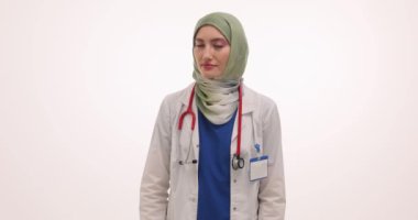 Tesettürlü kadın doktor, beyaz arka planda sessizlik istemek için parmağını dudaklarına kaldırır. Müslüman sıhhiyeden istişare sırasında sesi kısma talebi
