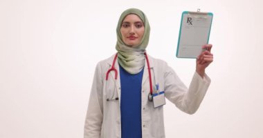 Gülümseyen Müslüman kadın doktor reçete formunda ve haplar su topladı. Başörtüsü uzmanı tıbbi tedavi uygular. Ağır çekim demektir.