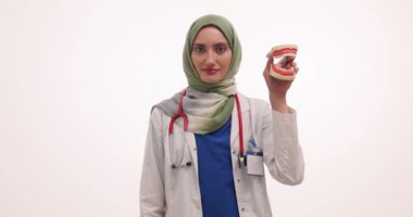 Müslüman kadın doktor diş modelini ve diş fırçasını gösteriyor. Türbanlı kadın hekim, uygun fırçalama tekniklerini gösteren ağız hijyenini vurguluyor