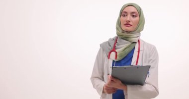 Müslüman kadın doktor elinde tıbbi kayıtlarla yön gösteriyor. Bayan hekim, muayene odasının yönünü göstermek için hasta detaylarını inceliyor.