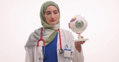 Steteskoplu Müslüman kadın doktor retinayı gösteren göz modelini tutuyor. Türbanlı kadın hekim, tıp öğrencilerine göz anatomisini öğretiyor
