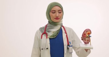 Müslüman kadın doktor böbrek modelini ve ilaçları su toplamış olarak gösteriyor. Türbanlı kadın doktor hastaya terapi ilacı yazıyor.
