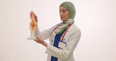 Steteskoplu Müslüman kadın doktor diz kemiği modelini gösteriyor. Kadın doktor eklem yapısının anatomisini açıkladı. Dizin plastik kopyası.