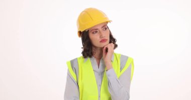 Şapkalı genç kadın mühendis iş perspektifini düşünürken çenesine dokunuyor. Yansıtıcı yelek içindeki konsantre kadın proje stratejisini formüle eder