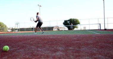 Yetenekli bir oyuncu canlı bir kırmızı kil sahada heyecanlı bir maç sırasında tenis topuna vurmaya hazırlanıyor.