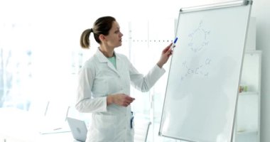 Bir bilim adamı parlak ve modern bir laboratuvar ortamında beyaz tahta kullanırken karmaşık kavramları tutkuyla açıklıyor.