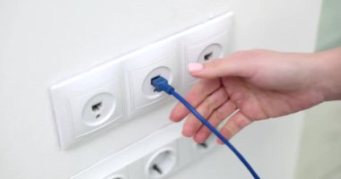 Bir el, güçlü bağlantıyı sembolize eden parlak mavi bir ethernet kablosunu bir duvar prizine dikkatlice yerleştiriyor.