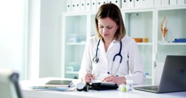 Kendini işine adamış ve odaklanmış bir kadın doktor, parlak ve modern bir tıp bürosundaki hasta kayıtlarını inceliyor.