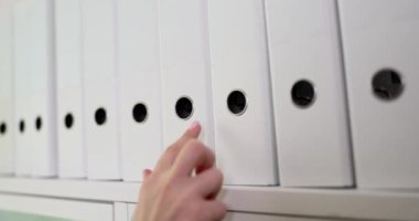 Bir el, düzenli bir ofis deposu eşyasının arasında el değmemiş beyaz bir klasöre uzanıyor.