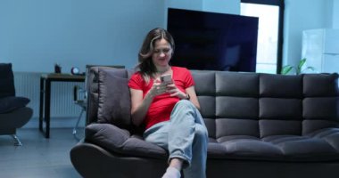 Bir kadın şık ve sakin bir ortamda akıllı telefonuyla dolu şık bir koltukta rahatça oturur.