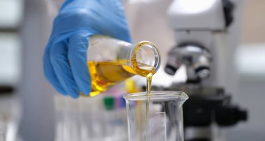 Eldivendeki bir el laboratuara sarı bir sıvı döküyor, yakın plan, bulanık. Optik mikroskop, idrar analizi