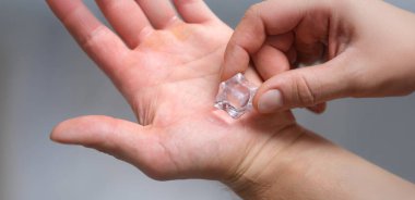 Bir el mısıra buz küpü sürer, yakın plan. Avuç içlerindeki kuru, pürüzlü deri, parmaklarındaki kabarcıklar yüzünden oluşan ağrı.