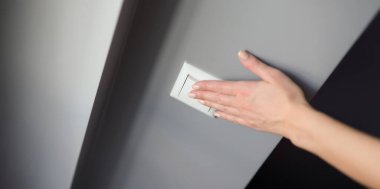 Bir kadının eli gri bir duvarda beyaz bir düğmeye basar, yakın plan. Elektrik ışığını kapatmak için aygıtlar