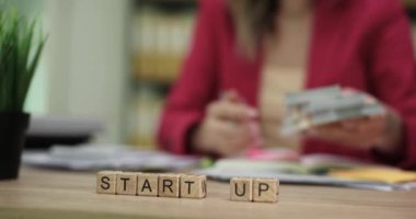 Profesyonel biri başlangıç stratejilerini tartışır, finansal belgeleri analiz eder ve resimleme için scrabble bloklarını kullanır