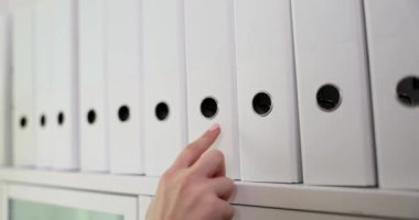 Düzenli ofis raflarından el yapımı beyaz klasörü seçen bir elin yakın çekimi.